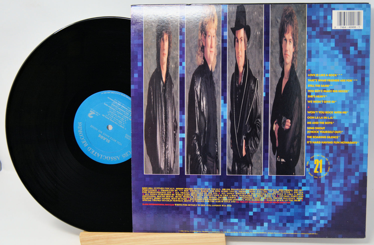 A vinyl record partially pulled from its sleeve, showing the black record with a blue center label and the back cover featuring four portrait photos of a band against a blue pixelated background.