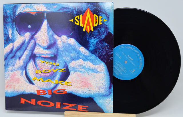 A vinyl record and its album cover for Slade's 'You Boyz Make Big Noise'. The cover features a stylized, high-contrast blue and pink portrait of the artist in sunglasses, with yellow and red text.