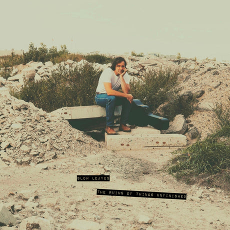 Person sitting with a guitar case in a rocky, desert-like landscape with text overlay.