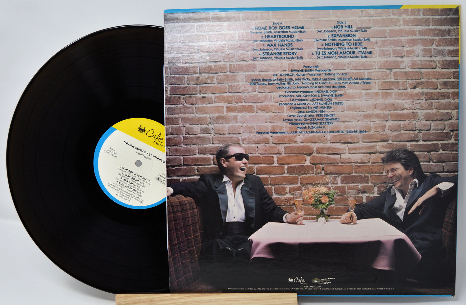 Vinyl record with cover featuring two people at a table against a brick wall.