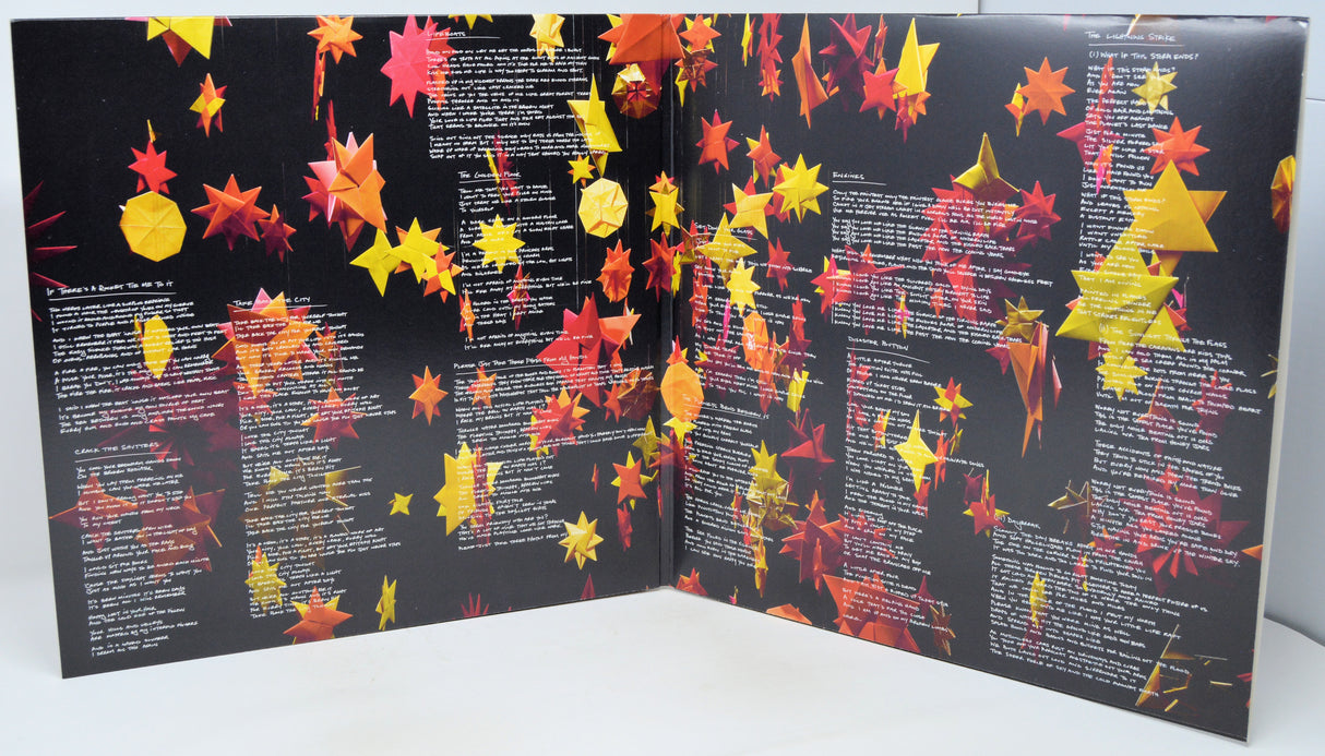 An open book or booklet with black pages covered in rows of white text and decorated with many hanging red, orange, and yellow paper-like leaves, photographed against a plain light background.
