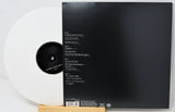 A vinyl record partially pulled from its black outer sleeve, photographed on a white background with a small wooden stand visible at the bottom.