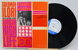 Vinyl record with a colorful cover featuring text and images, on a light gray background.