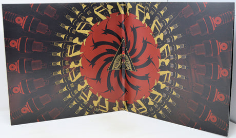 A folded vinyl record sleeve or album cover featuring a central red circular design with black spiral shapes and a gold triangle logo, surrounded by a black background with repeating red and gold mechanical illustrations.