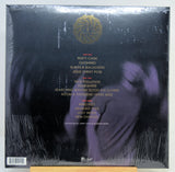 The back cover of a vinyl record in its shrink wrap, featuring a black background with gold tracklist text and a gold circular logo at the top.