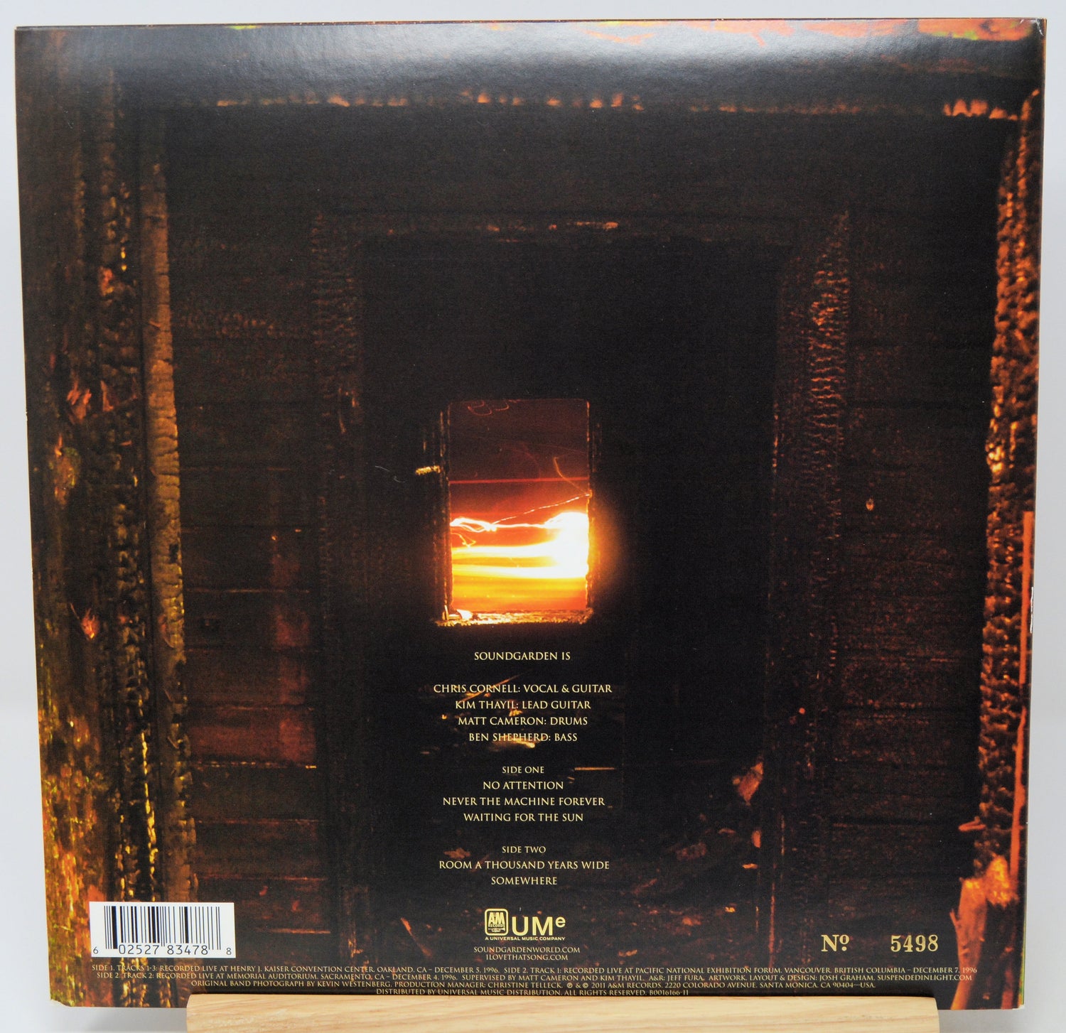 The back cover of a vinyl record for Soundgarden's album 'Showbizgenial', featuring a dark, fiery scene with a glowing orange window and tracklist text, displayed on a wooden stand.