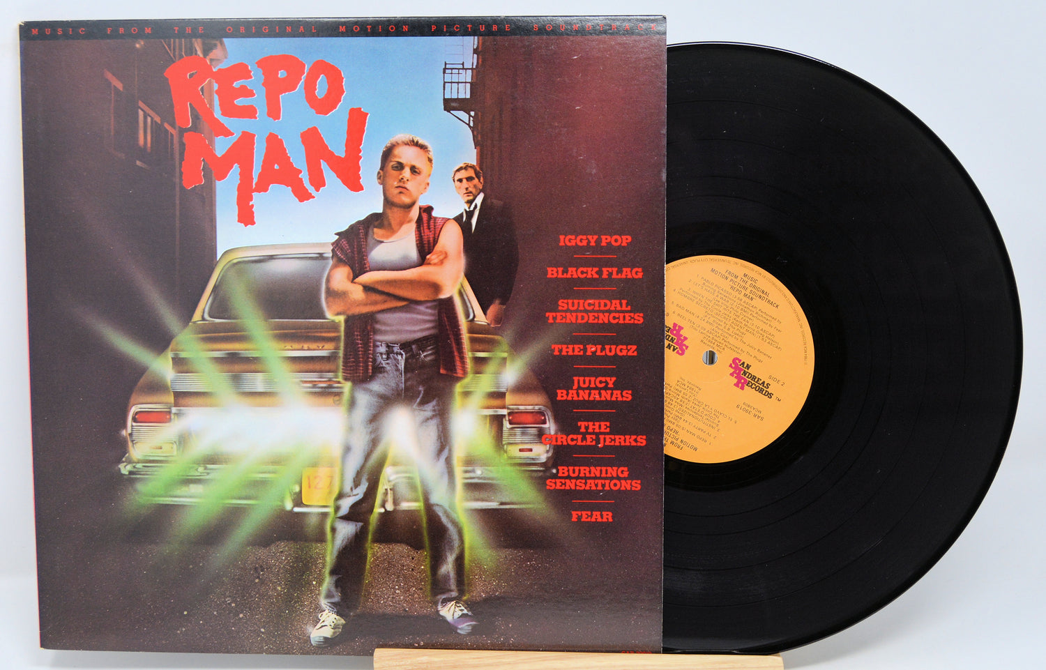 Used vinyl record of 'Repo Man' soundtrack with album cover featuring a man in a tank top and jeans, standing with his hand on a car, against a neon-lit background. The record label is visible with the text 'SAN ANTONIO RECORDS SAR 39019'.