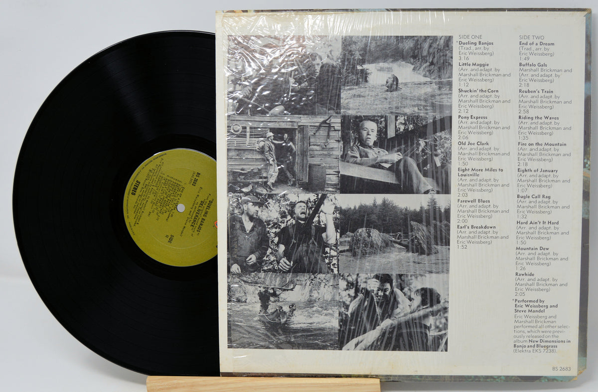 A vinyl record partially pulled from its sleeve, showing the black record with a yellow label next to the printed back cover artwork and tracklist on a white background.