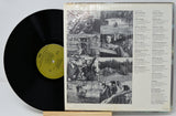 A vinyl record partially pulled from its sleeve, showing the black record with a yellow label next to the printed back cover artwork and tracklist on a white background.