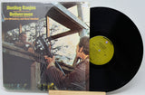 Deliverance Duoline Canjos vinyl record LP with its illustrated cover jacket and black record partially pulled out, displayed on a small wooden stand against a light gray background.