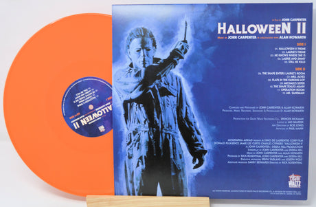 Vinyl record with orange disc and blue cover featuring a silhouette of a character holding a knife, on a white background.