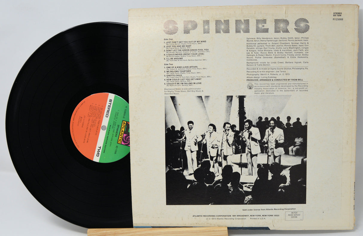 Vinyl record with cover featuring a group of people and text, on a light gray background.