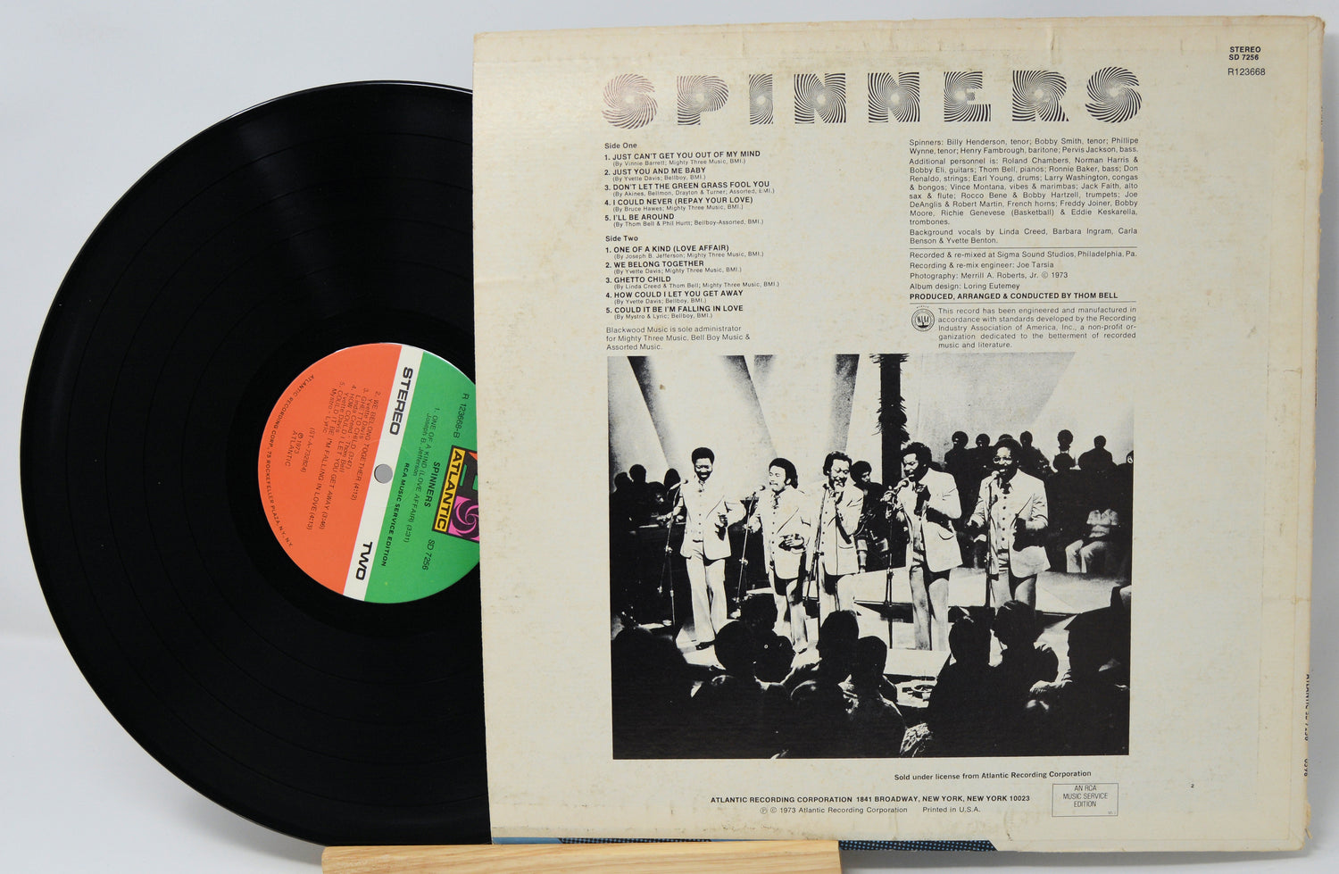 Vinyl record with cover featuring a group of people and text, on a light gray background.