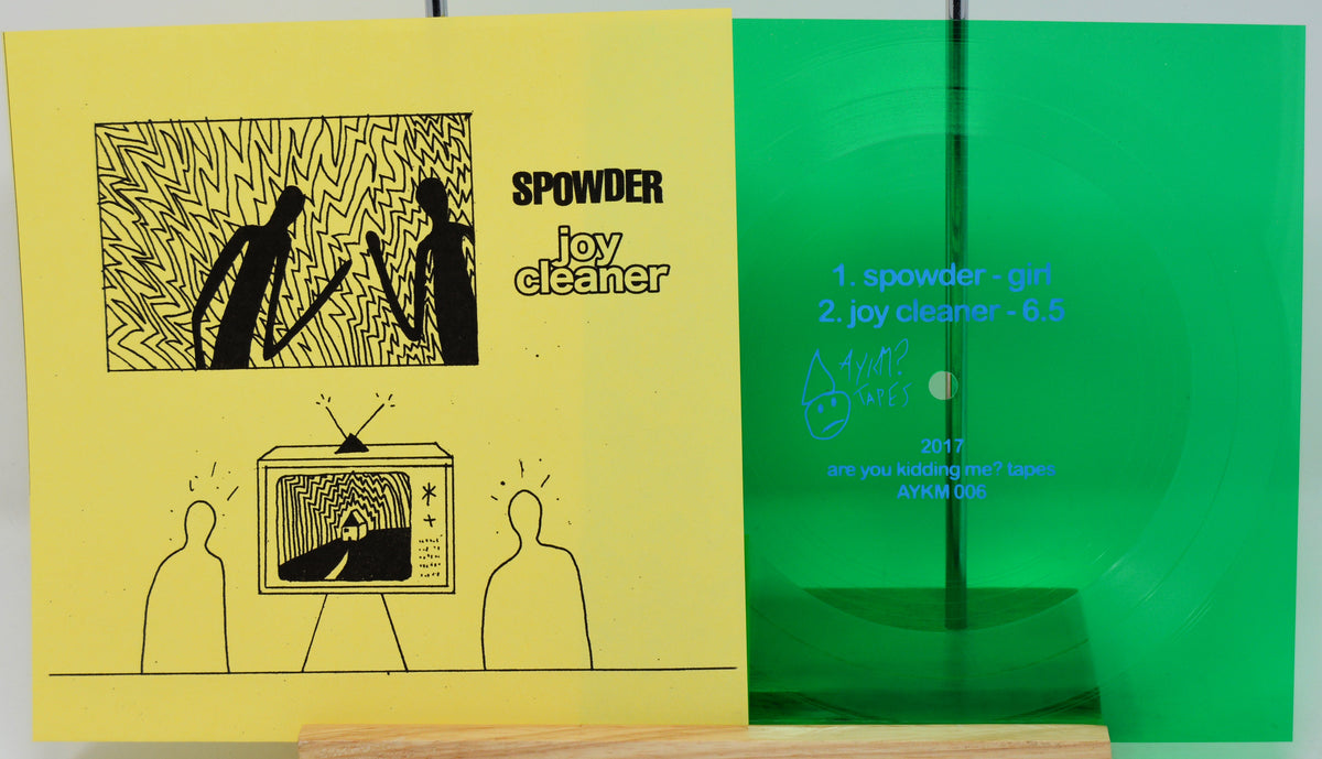 A vinyl record package shown flat against a white background, featuring a yellow cover with black line art and the text 'SPOWDER joy cleaner,' alongside a bright green translucent record and track listing details.