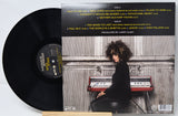 Vinyl record with a cover featuring a person playing an keyboard, on a light gray background.