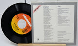 Vinyl record with Columbia label and record cover displaying tracklist on a white background