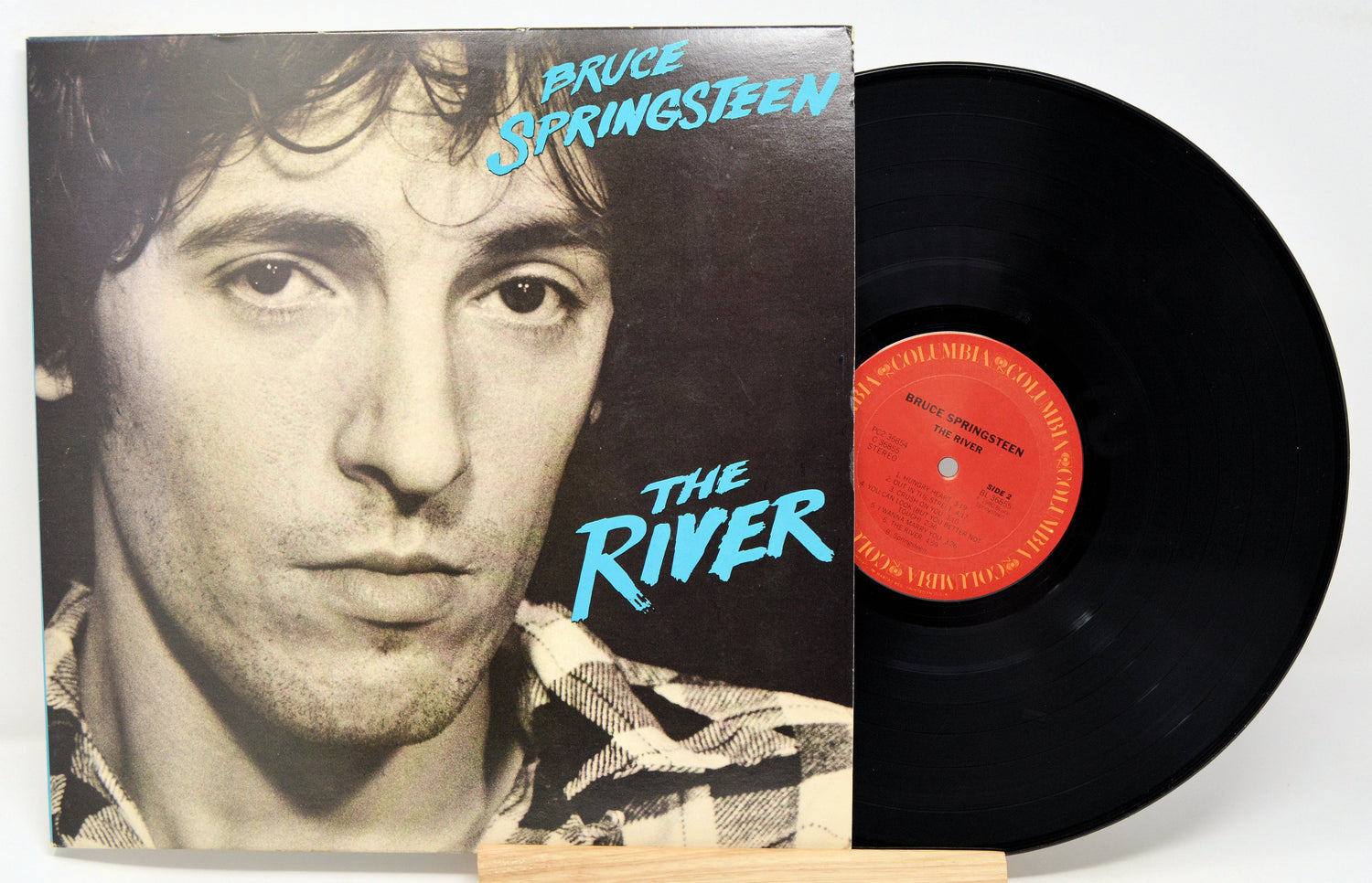 A used vinyl record of Bruce Springsteen's album 'The River' with the artist's photo on the cover, displayed alongside the black vinyl record.