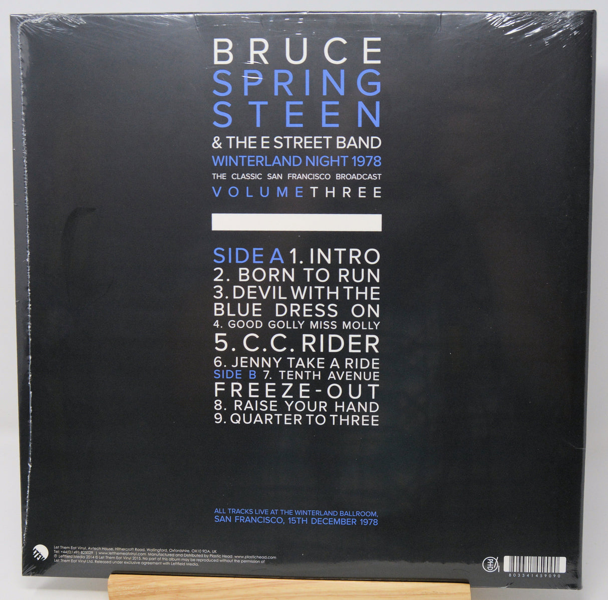 The back cover of a Bruce Springsteen & The E Street Band vinyl record, titled 'Winterland Night 1978: The Classic San Francisco Broadcast Volume Three'. The cover is black with white and blue text, wrapped in clear plastic, and photographed resting on a light-colored wooden stand.