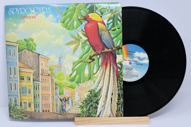 Used vinyl record of Spyro Gyra's album Carnaval with a colorful bird on the cover, set against a background suggesting a lush landscape with buildings.