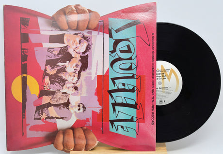A vinyl record partially pulled from its sleeve, held by hands against a light gray background. The sleeve features a pink and red graphic cover with the word 'LOQUEE' in large stylized letters, and the black record is visible behind it.