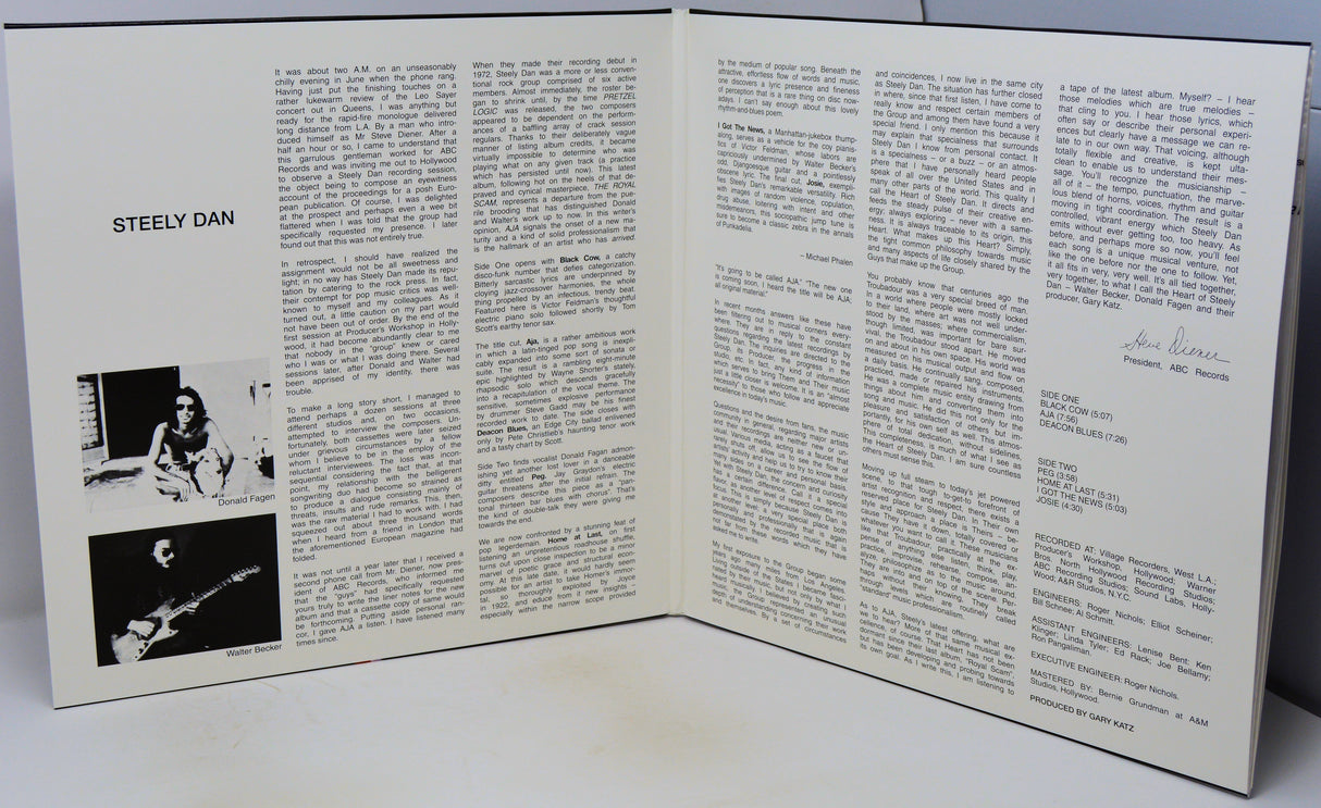 An open printed booklet or magazine spread showing two white pages with columns of black text, a photo labeled 'STEELY DAN' on the left page, and a signature on the right page, photographed on a light surface.