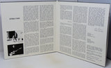 An open printed booklet or magazine spread showing two white pages with columns of black text, a photo labeled 'STEELY DAN' on the left page, and a signature on the right page, photographed on a light surface.