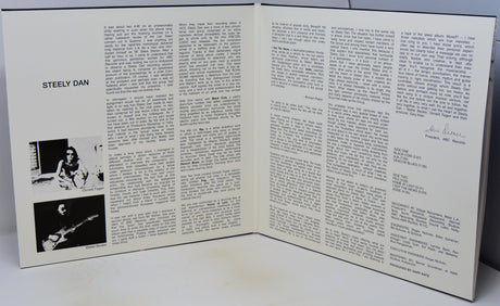 An open printed booklet or magazine spread showing two white pages with columns of black text, a photo labeled 'STEELY DAN' on the left page, and a signature on the right page, photographed on a light surface.