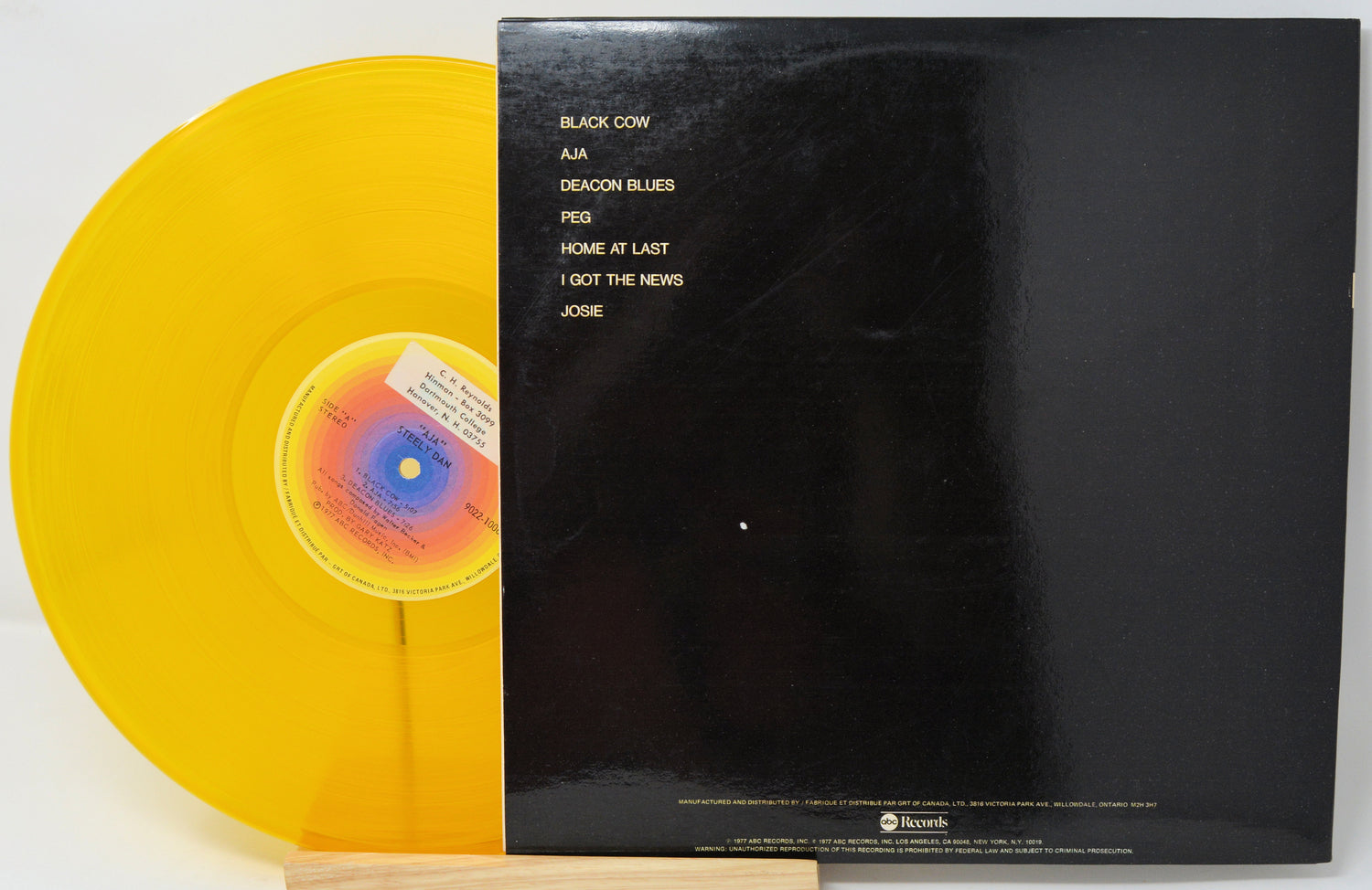 A vinyl record partially pulled from its black sleeve, showing a translucent yellow record and the back cover with tracklist text.