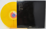 A vinyl record partially pulled from its black sleeve, showing a translucent yellow record and the back cover with tracklist text.