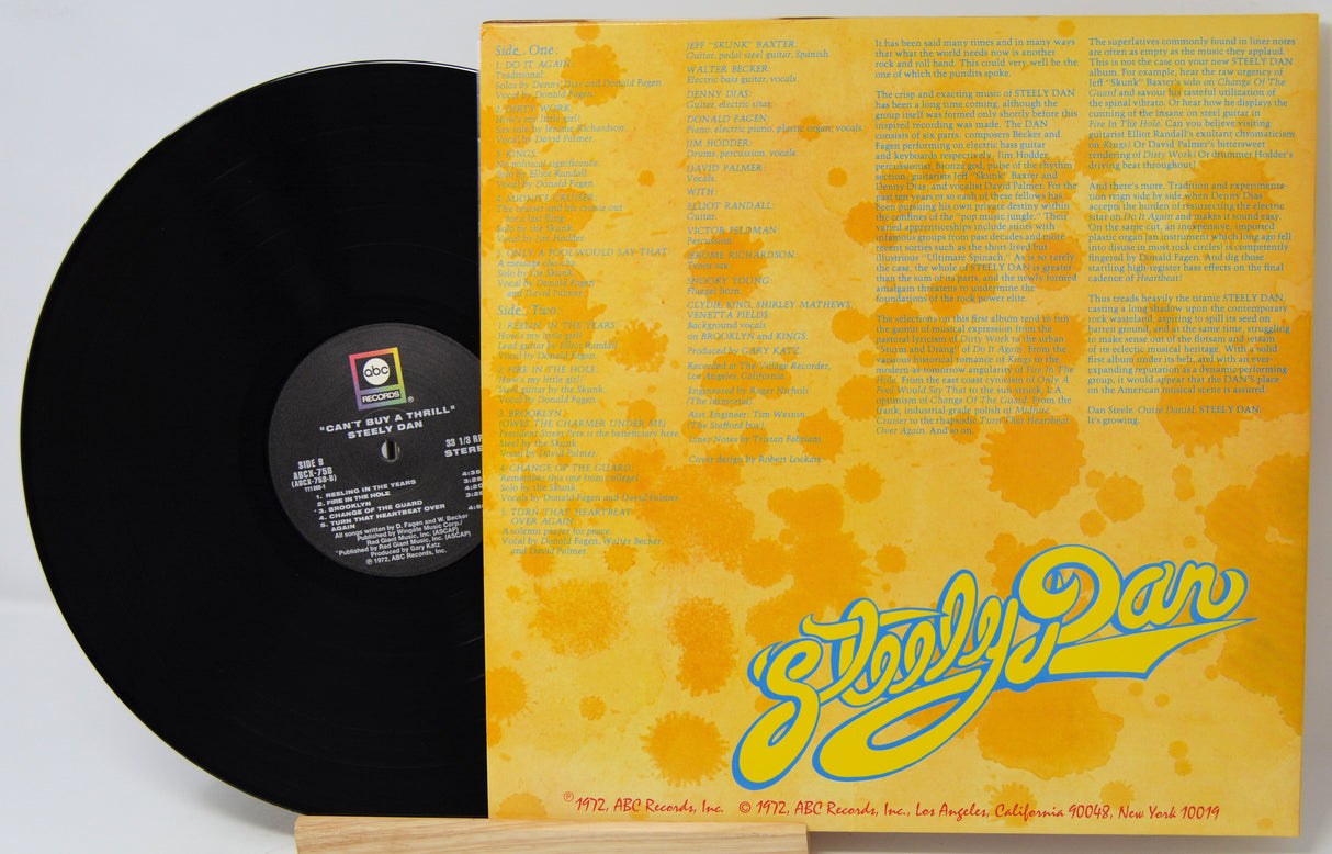 A vinyl record partially pulled from its sleeve, showing the black record on the left and the yellow cover on the right with blue and orange text and splatter graphics. The record label reads 'Hazy E.