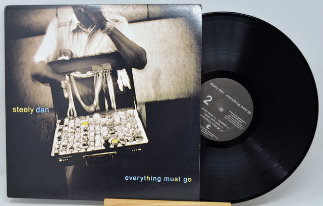 Steely Dan's 'Everything Must Go' vinyl record LP shown with its album cover in front of the black record on a light gray background.