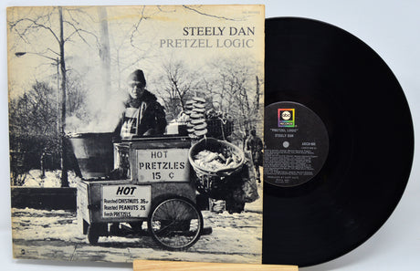 Vinyl record with 'Steely Dan Pretzel Logic' cover showing a black and white image of a hot pretzel vendor.
