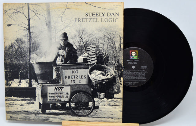 Vinyl record with 'Steely Dan Pretzel Logic' cover showing a black and white image of a hot pretzel vendor.