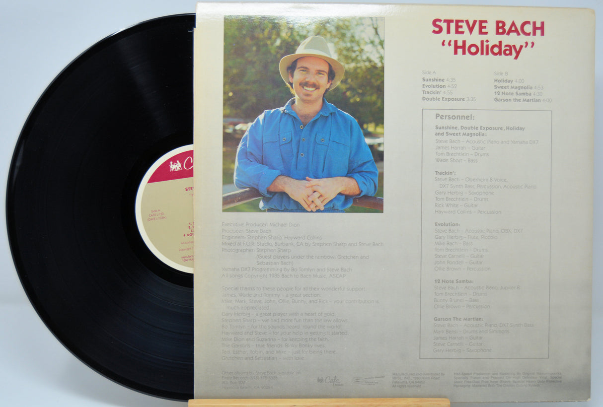 Vinyl record with cover featuring a man in a blue shirt and hat, titled 'Holiday' by Steve Bach.
