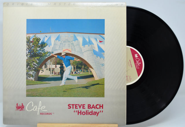 Vinyl record with cover featuring a man in a blue shirt and white pants, titled 'Holiday' by Steve Bach.