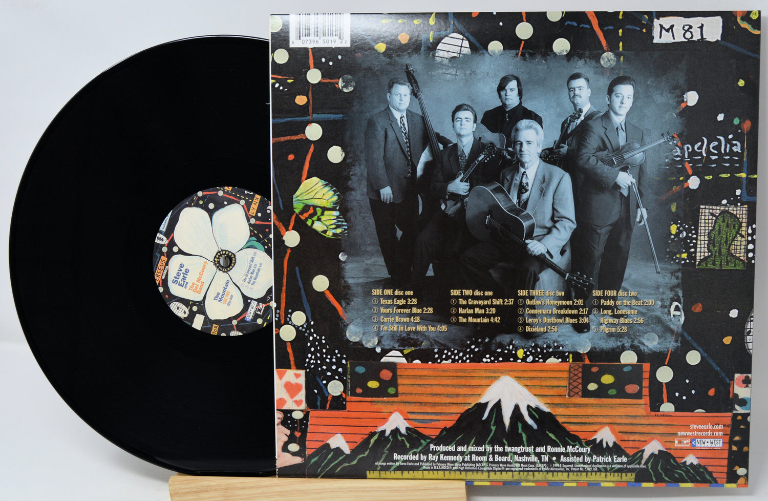 A vinyl record partially pulled from its illustrated outer sleeve, showing the black record and the back cover artwork with a band photo and colorful abstract graphics.