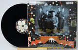 A vinyl record partially pulled from its illustrated outer sleeve, showing the black record and the back cover artwork with a band photo and colorful abstract graphics.