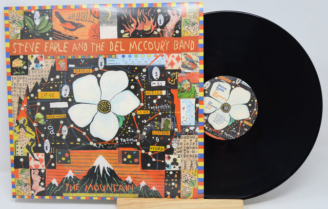 Steve Earle and the Del McCoury Band's 'The Mountain' vinyl record LP, showing the illustrated album cover sleeve and the black vinyl record partially pulled out, displayed on a small wooden stand against a light gray background.