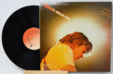 Steve Miller Band vinyl record LP with the black record partially pulled from its illustrated album cover, which features a warm-toned portrait of a person and orange text, displayed on a small wooden stand.