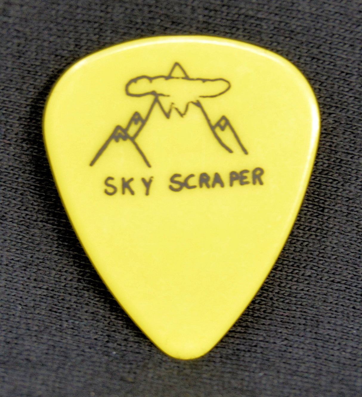 Yellow guitar pick with 'Sky Scraper' design on a black textured background
