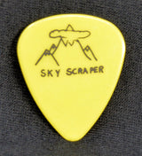 Yellow guitar pick with 'Sky Scraper' design on a black textured background