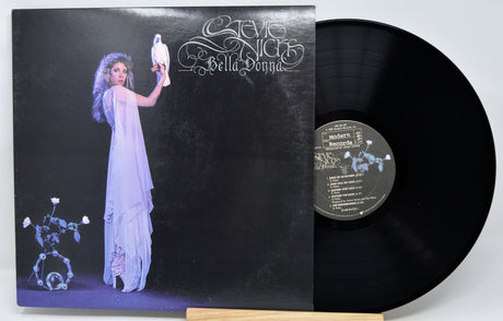 Steve McQueen's 'Bella Donna' vinyl record LP with its illustrated cover jacket and the black vinyl disc partially pulled out, displayed on a small wooden stand against a light gray background.