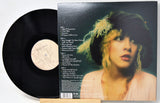 Vinyl record album shown with the black LP partially pulled from the sleeve, which features a printed track listing and a portrait of a woman with blonde hair and a dark hat.