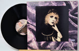 Vinyl record with a stylized cover featuring a person's portrait and decorative elements.