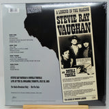 The back cover of a Stevie Ray Vaughan double-sided vinyl record, sealed in plastic shrink wrap, displayed on a wooden stand against a white background.