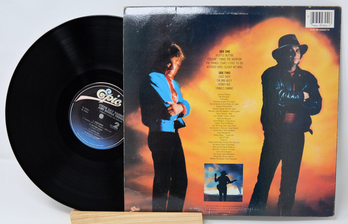 Vinyl record 'Stevie Ray Vaughan Couldn't Stand The Weather'  with cover featuring a person in a blue jacket and hat against an orange sky.
