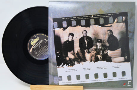 A vinyl record partially pulled from its sleeve, showing the black record and the printed cover art. The sleeve features a film-strip design with a black-and-white band photo and text for the album 'The Great Escape'.