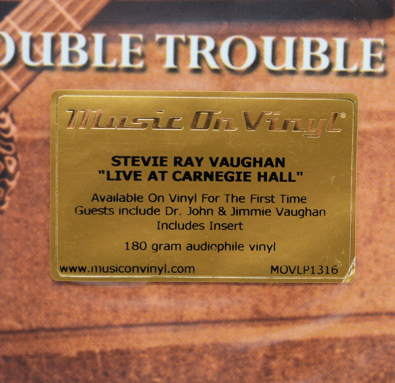 A gold-colored rectangular label on the front of a Stevie Ray Vaughan 'Live at Carnegie Hall' vinyl record package, with 'Music On Vinyl' branding and product details printed on it.