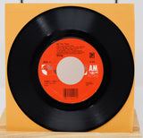 A vinyl record of Sting's song 'All This Time' with a visible orange and white label, placed on a yellow surface.