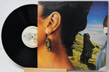 Vinyl record album with the black record partially pulled from the sleeve, showing the cover art of a woman's ear wearing a dangling stone earring against a grassy landscape background.